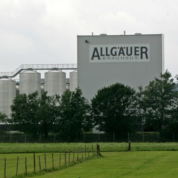 Großes Industriegebäude und Silos stehen hinter einer Wiese mit Zaun.