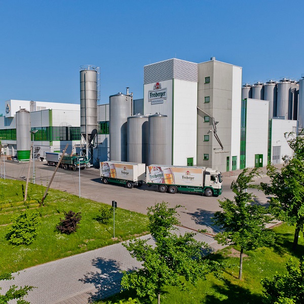 Eine große Industrieanlage mit Silos und LKW ist unter blauem Himmel abgebildet.