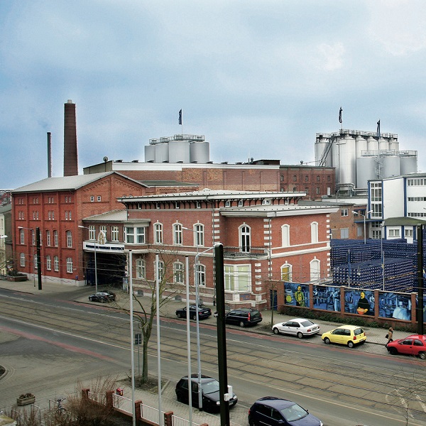 Altes Industriegebäude in rotem Backstein mit modernen Anbauten an einem bewölkten Tag.