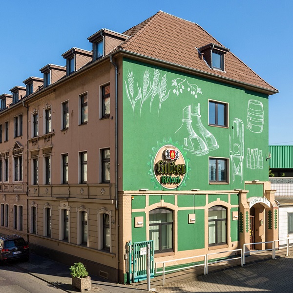 Ein grünes Eckgebäude mit Gaststätte im Erdgeschoss zeigt landwirtschaftliche Wandmalereien.