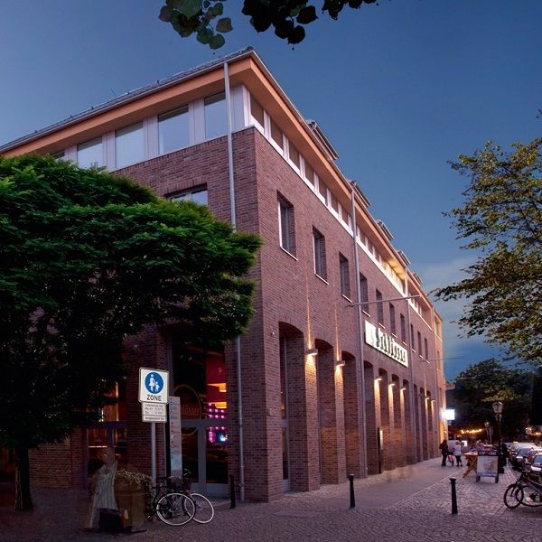 Ein dreistöckiges rotes Backsteingebäude bei Dämmerung mit beleuchteten Fenstern.