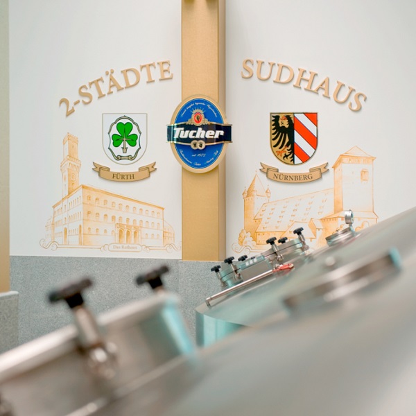 Eine Wand mit Stadtwappen und dem Schriftzug 2 Städte hinter Bierfässern.