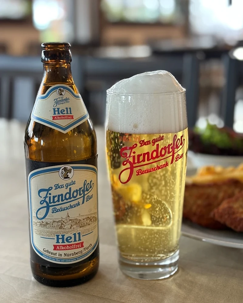 Eine Flasche und ein Glas gefüllt mit hellem, alkoholfreiem Bier stehen auf einem Tisch.
