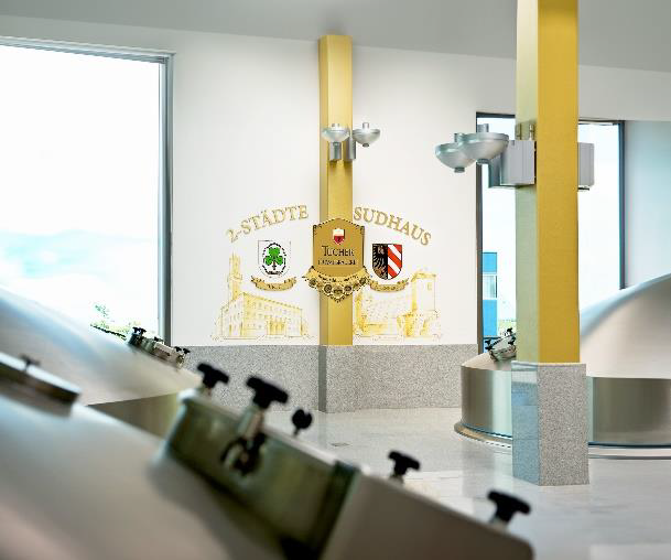 Ein moderner Brauerei-Innenraum mit zwei Bierhähnen im Vordergrund und Wappen auf Schildern im Hintergrund.