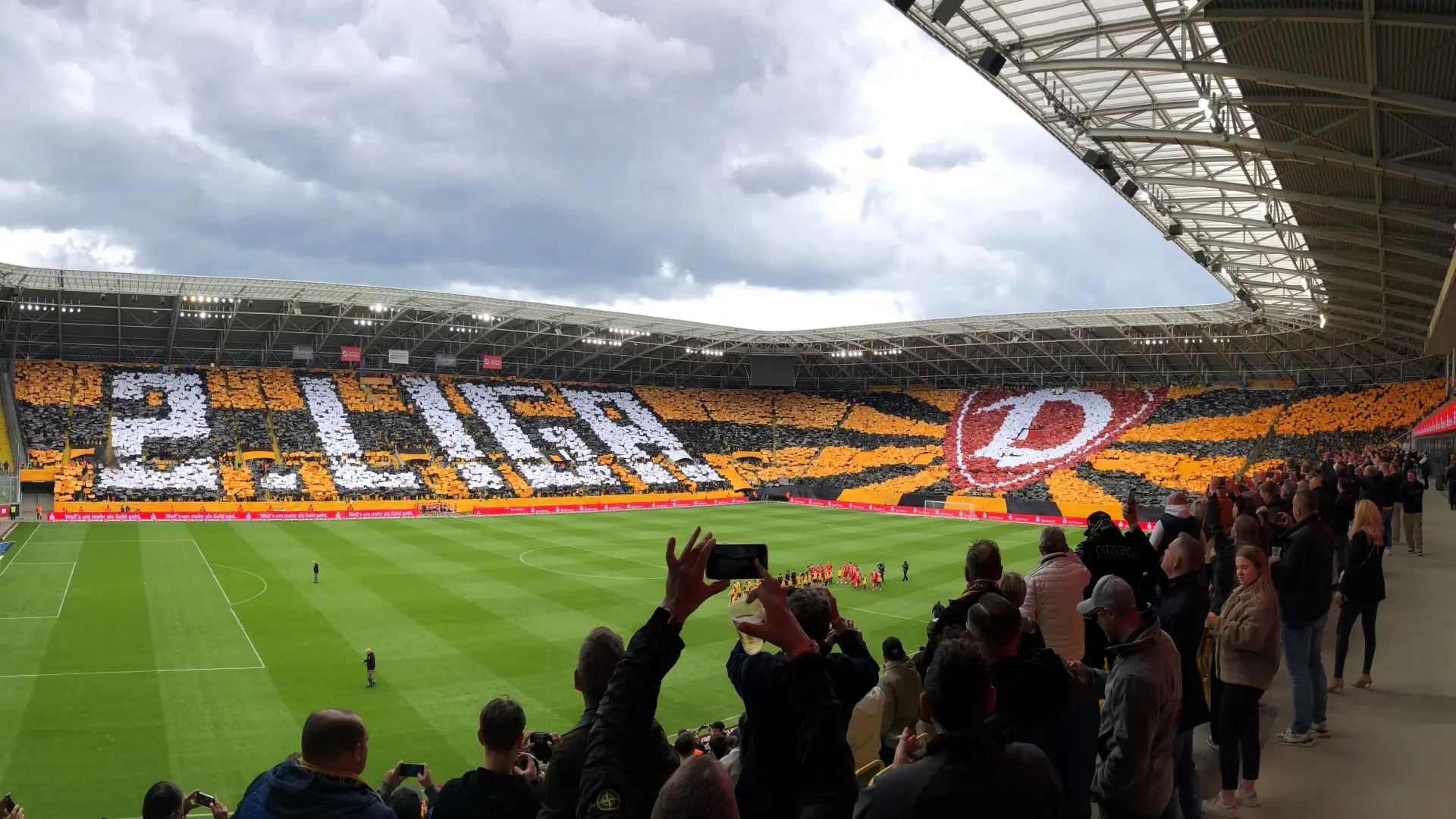 Ein Stadion mit Zuschauern, die einen bunten Sitzplatzmosaik inklusive einem großen Logo gestalten.