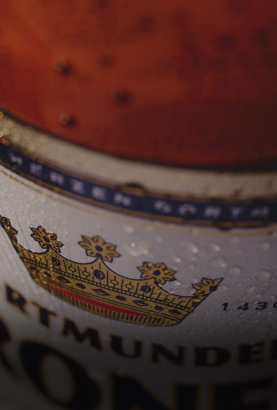Nahaufnahme eines Bierglases mit einem Wappen und Wassertropfen darauf. Der Hintergrund zeigt eine unscharfe orange Fläche.