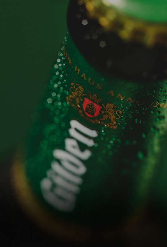 Nahaufnahme einer grünen Flasche mit Tropfen und goldener Kappe.
