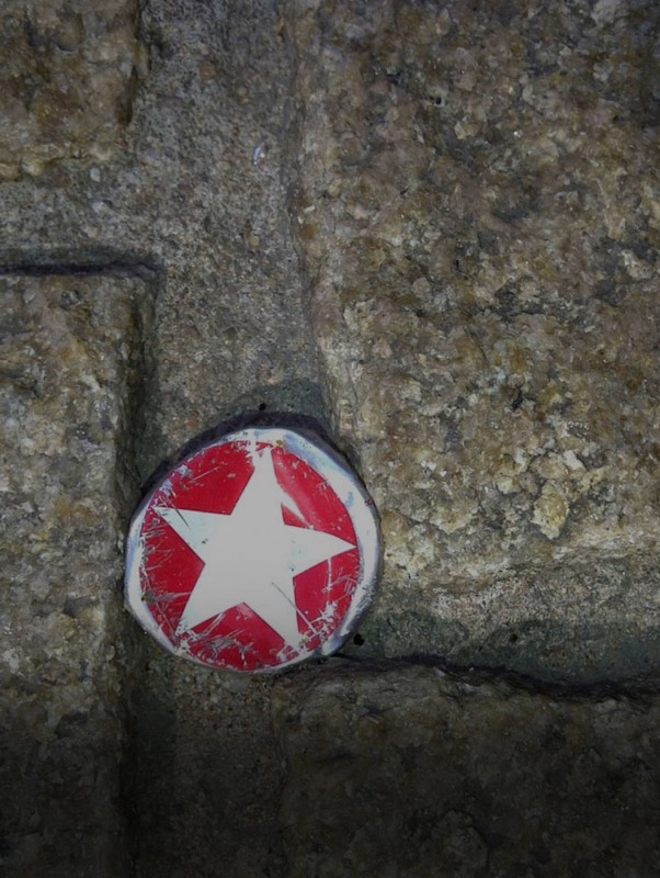 Ein abgenutzter, runder Gegenstand mit rotem Stern auf Pflastersteinen liegt im Fokus.
