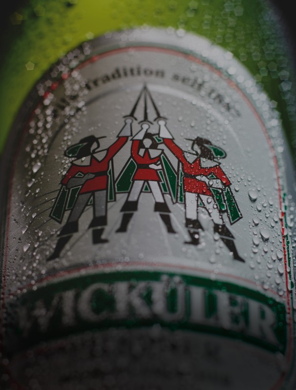 Nahaufnahme eines Bieretiketts mit drei Personen in traditioneller Kleidung unter einem Logo.