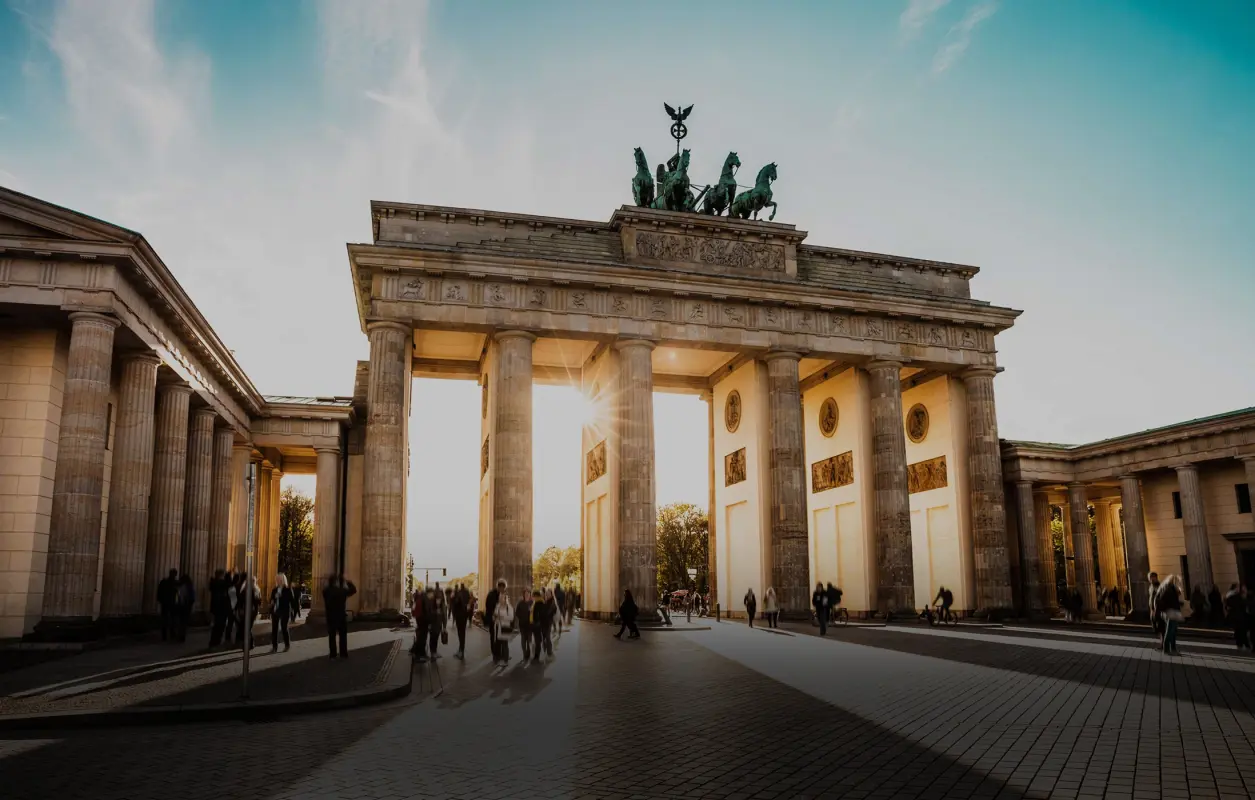 Sonnenlicht scheint durch die Säulen des Brandenburger Tors in Berlin, Menschen gehen vorbei.