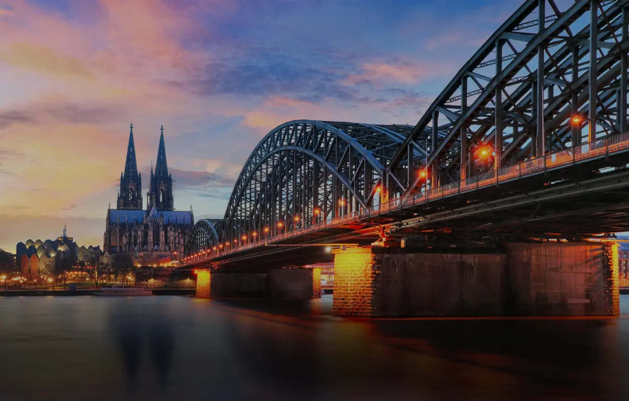 Eine stählerne Brücke führt über einen Fluss zu einer gotischen Kathedrale bei Sonnenuntergang.
