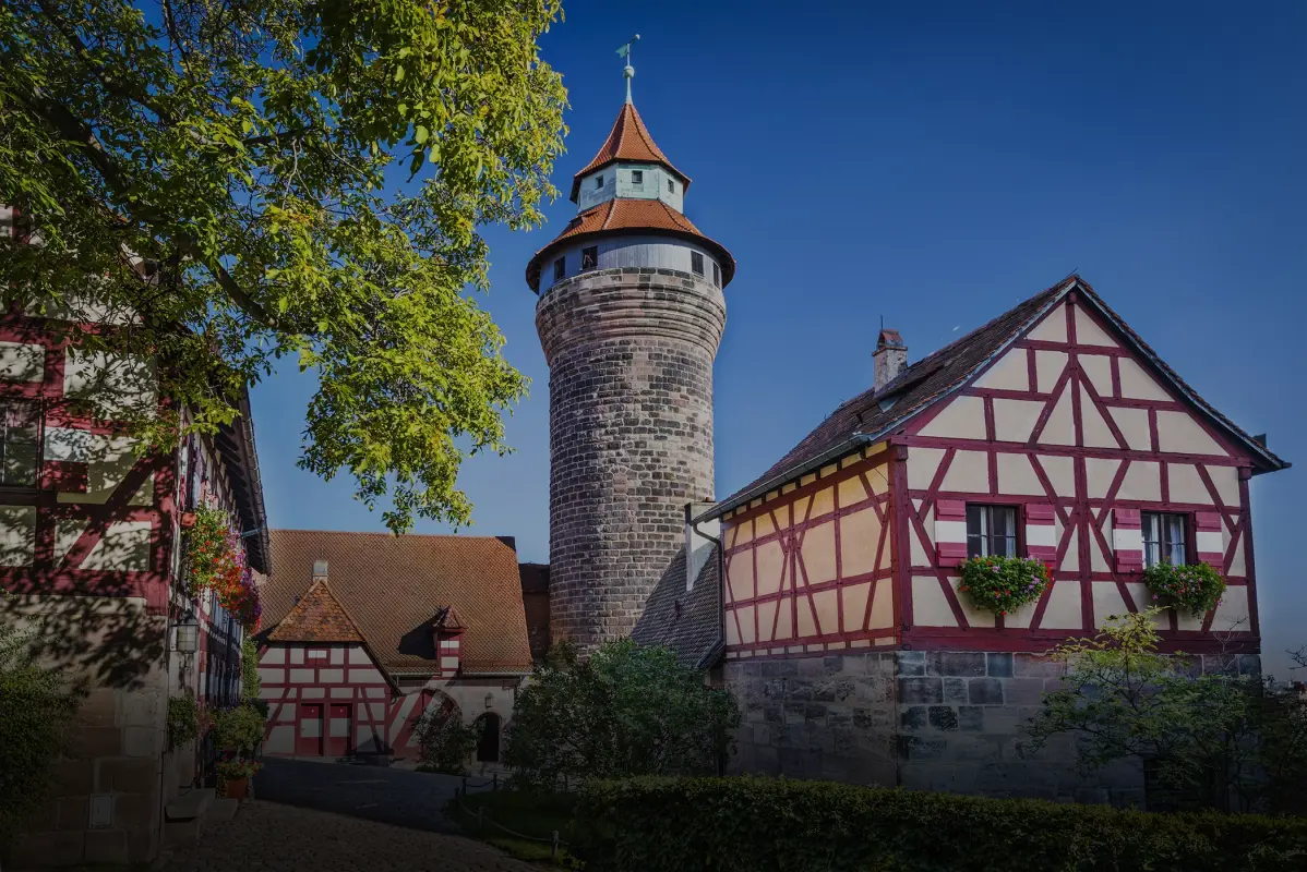 Ein Rundturm und ein Fachwerkhaus befinden sich in einem idyllischen Hof unter blauem Himmel.
