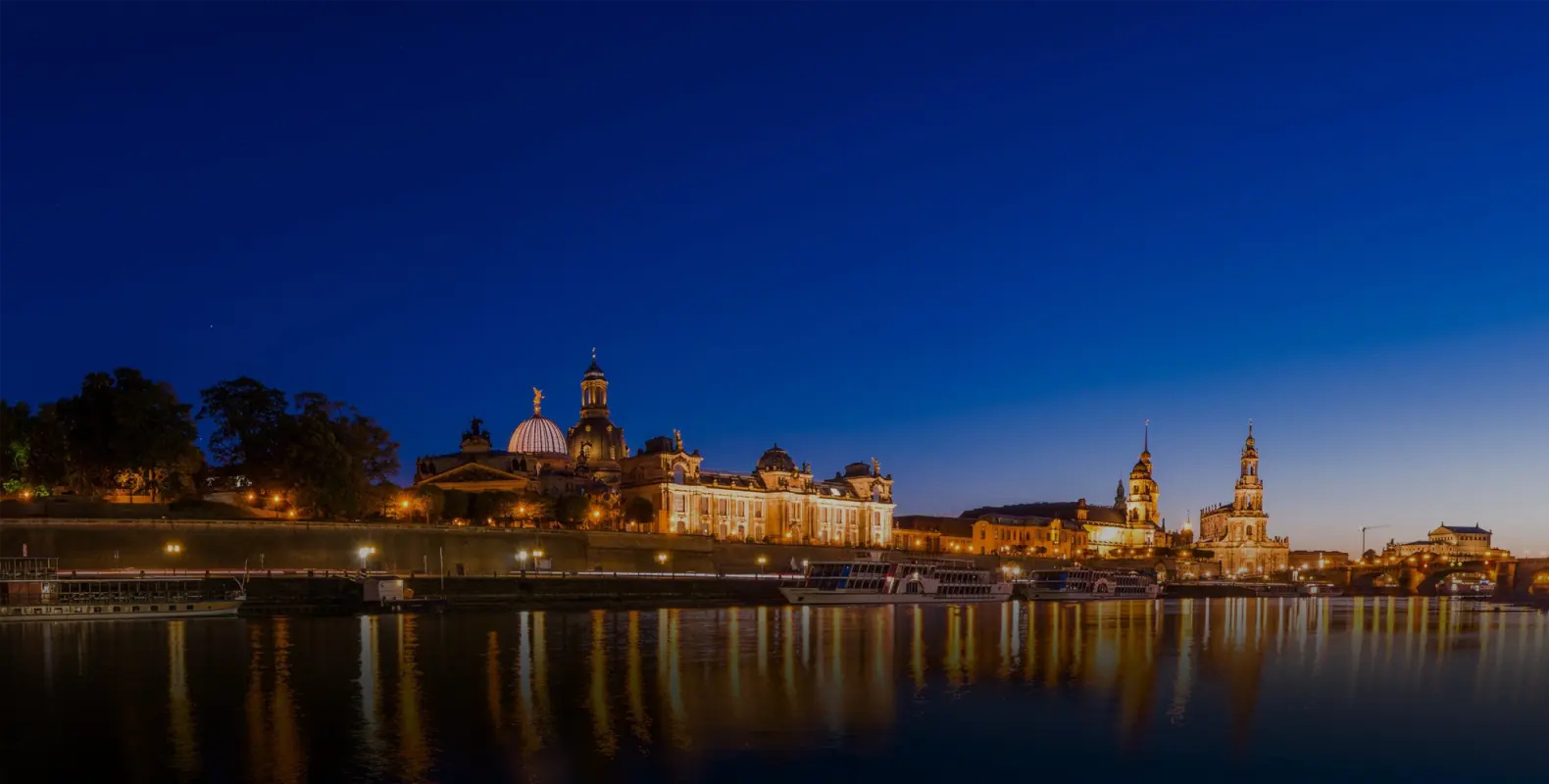 Historische Gebäude spiegeln sich bei Nacht in einem Fluss. Ihre Beleuchtung erzeugt glitzernde Reflexionen auf dem Wasser.
