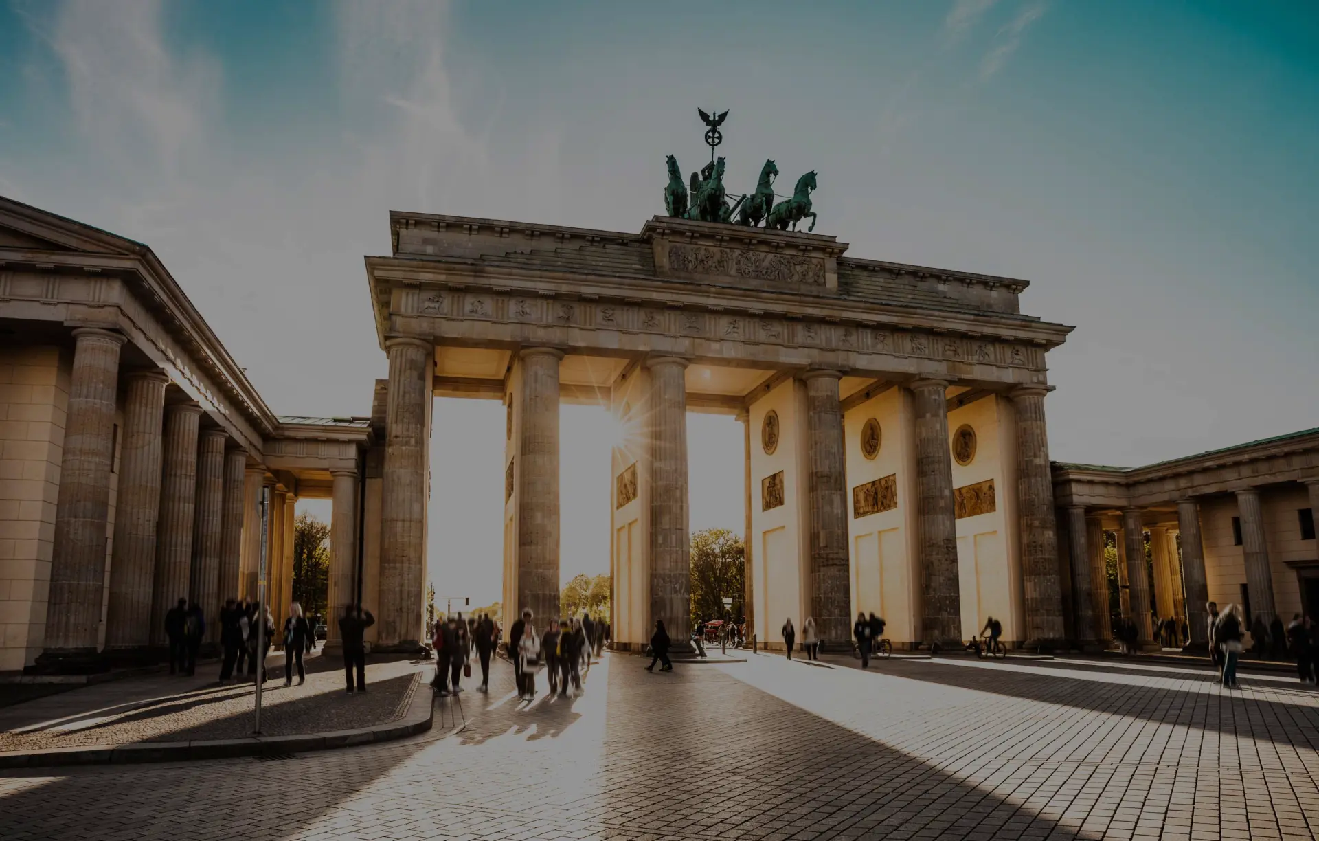 Brandenburger Tor mit Säulenreihe und Quadriga auf dem Dach. Menschen stehen auf dem Platz vor dem Bauwerk.