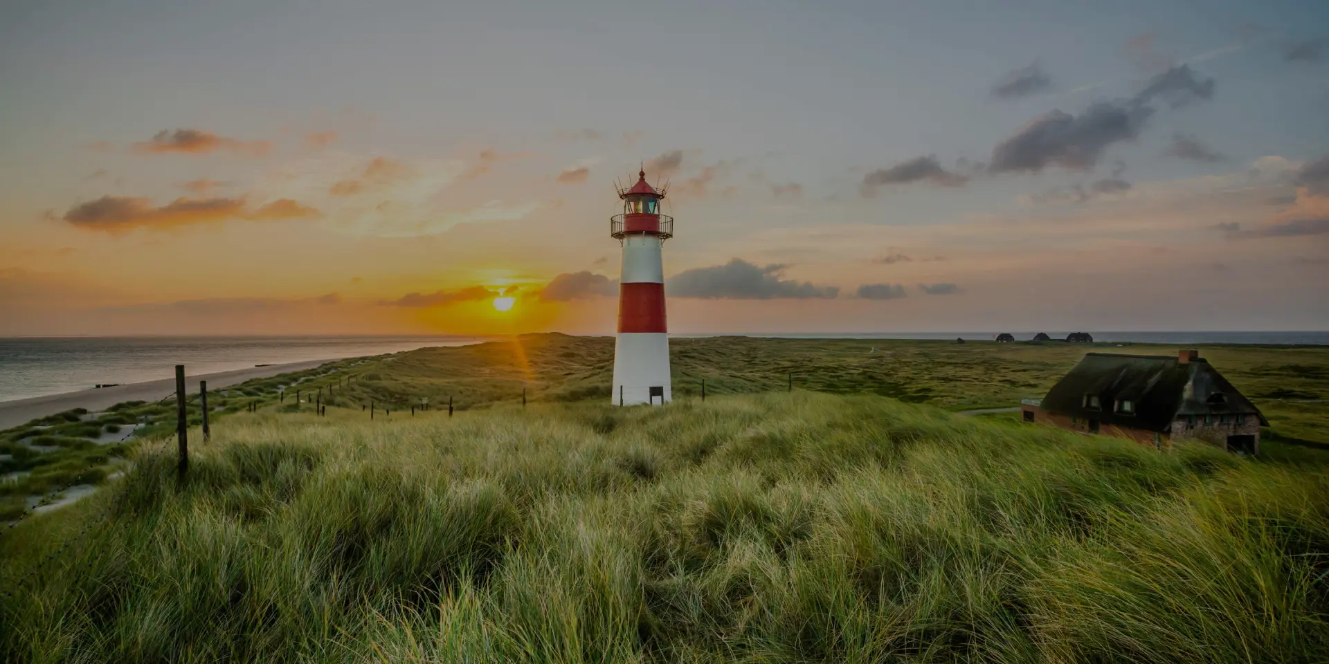 Leuchtturm steht auf einer Dünenlandschaft an der Küste. Meer und Himmel erstrecken sich bis zum Horizont.