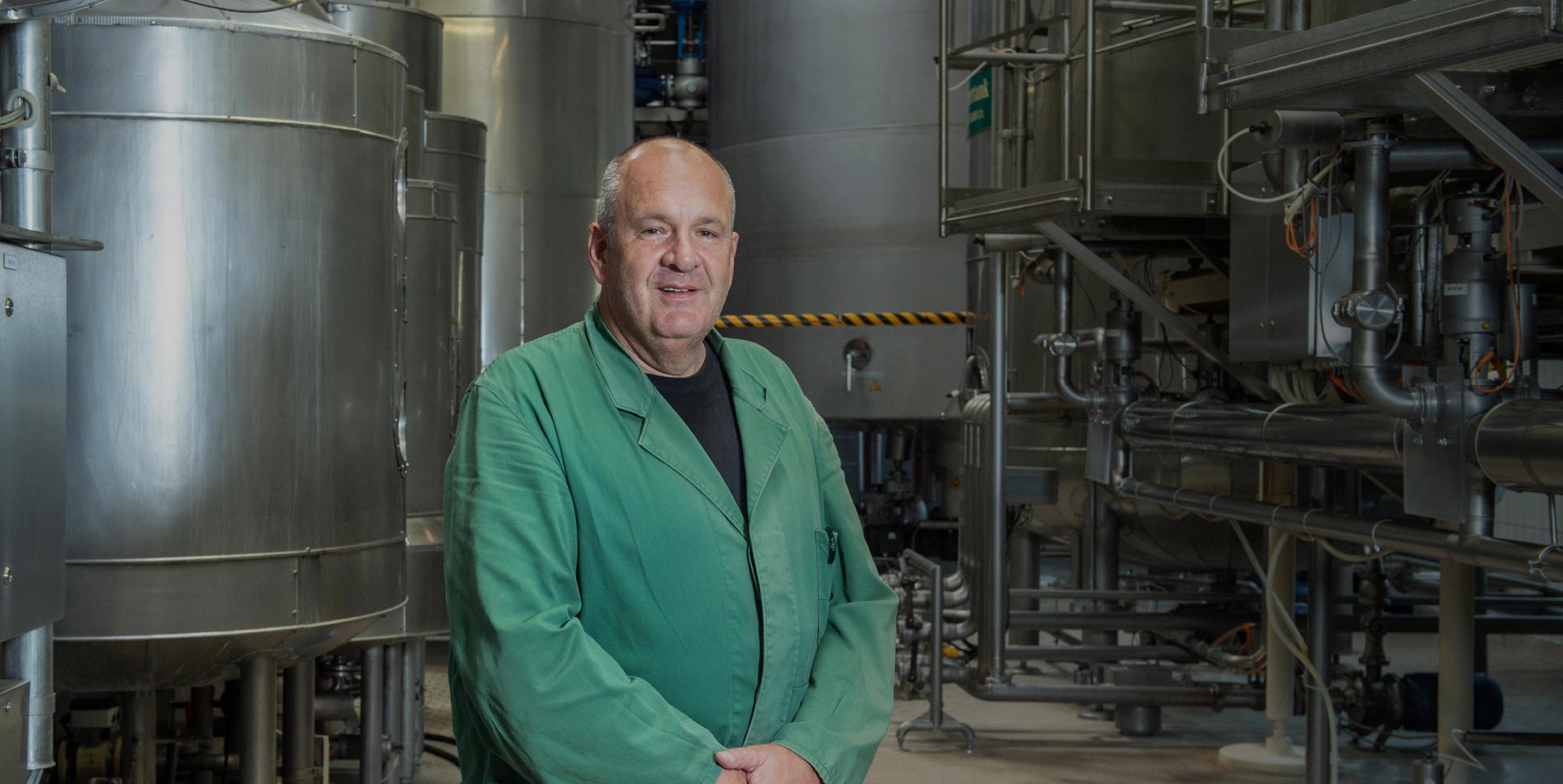 Ein Mann in grüner Arbeitskleidung steht vor großen Metalltanks in einer Fabrikhalle.
