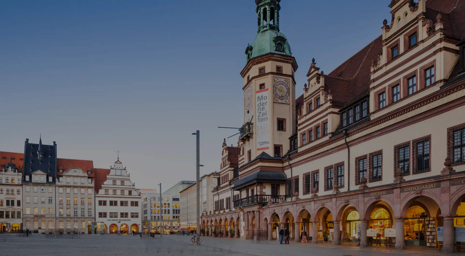 Historisches Gebäude mit Uhrturm prägt einen weiten Marktplatz. Weitere Häuser stehen entlang des Platzes.