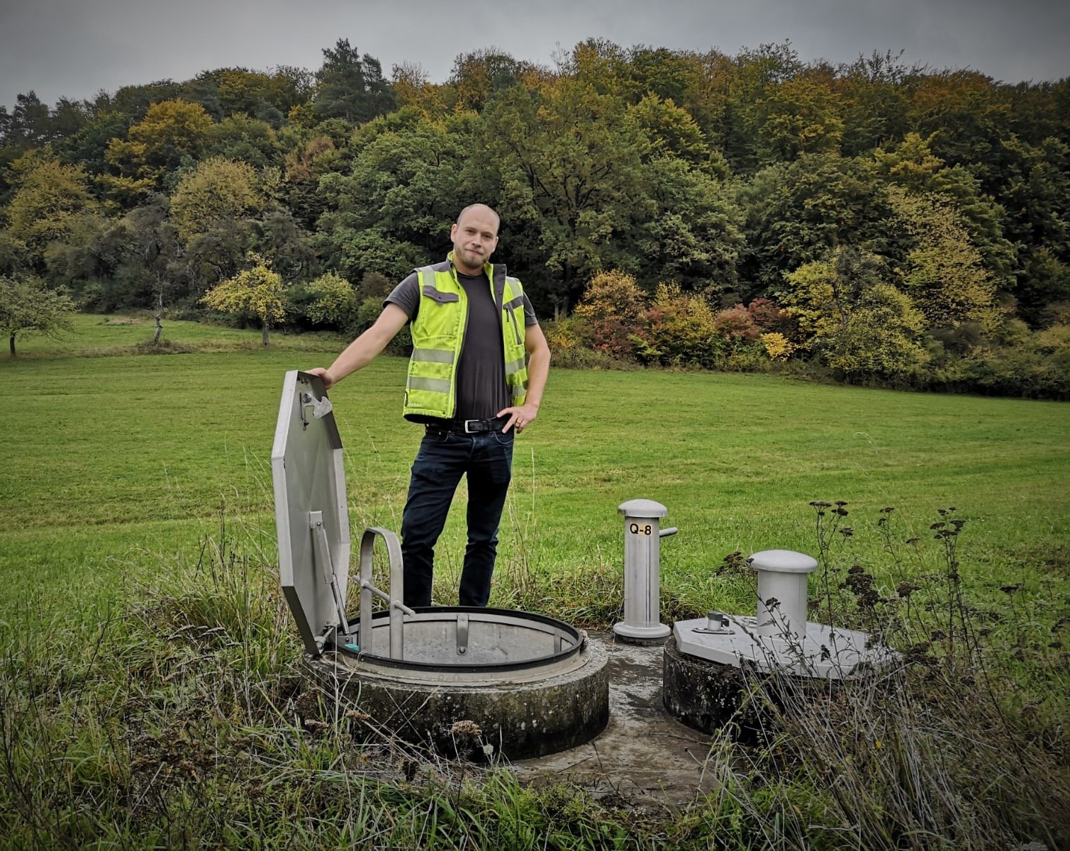 Ein Mann in Warnweste steht neben Metalldeckeln im Grünen.